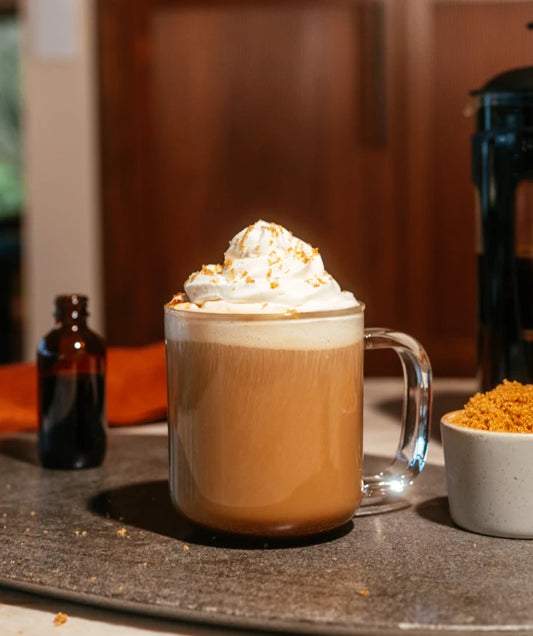 Hot Roasted Crème Brûlée with whipped cream on a wooden table with coffee beans and a coffee machine in the background.