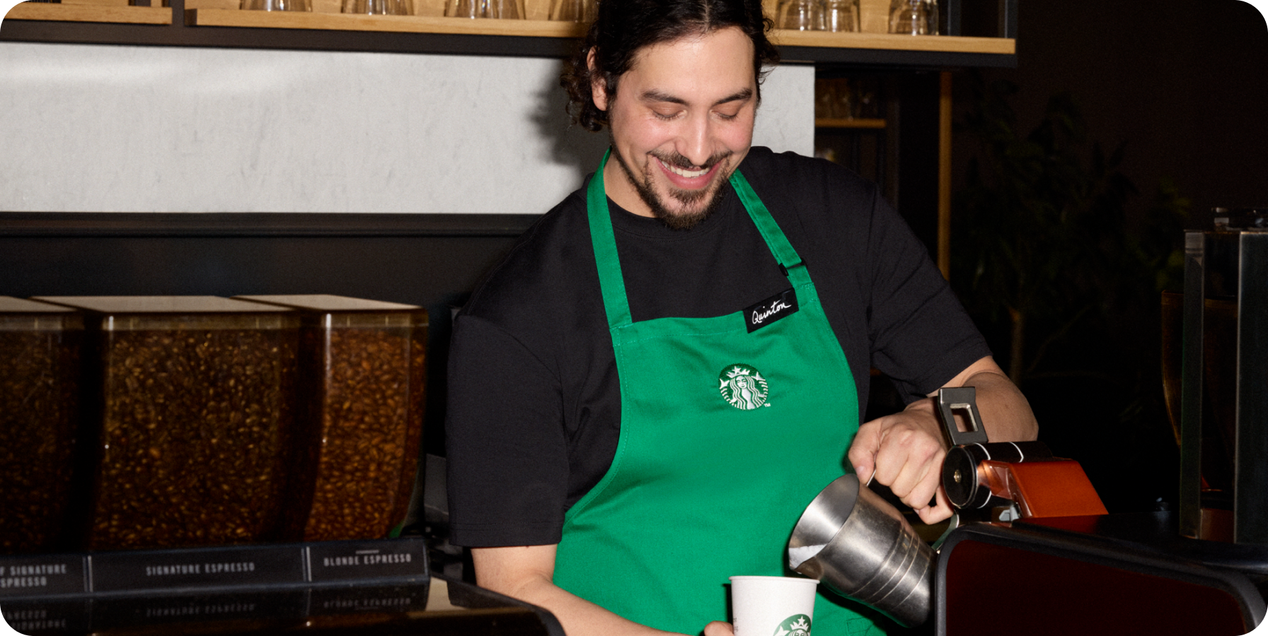 Barista in a Starbucks green apron preparing a coffee at a counter.