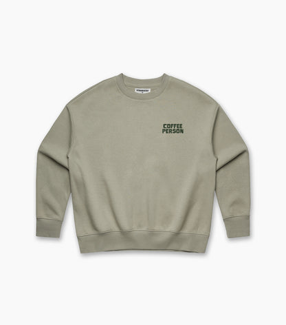 Front view of an olive-green women’s crewneck sweatshirt featuring a small ‘COFFEE PERSON’ graphic printed on the left chest.