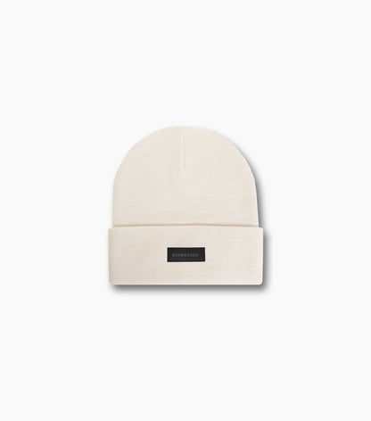 The front of the natural beige Starbucks Knit Beanie with a black Starbucks logo label, against a white background.