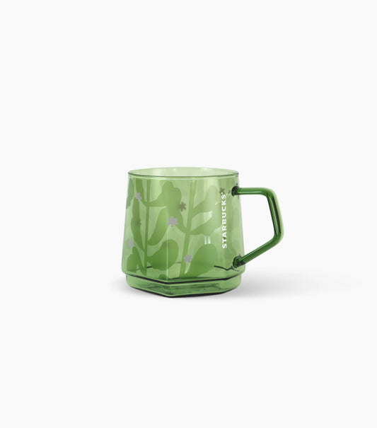 A translucent green glass mug with a matching green handle, featuring a subtle floral pattern and the vertical Starbucks logo on the side, set against a plain white background.