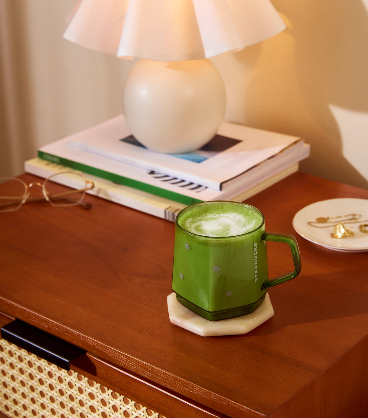 Green mug with a beverage on a wooden surface with books and glasses.