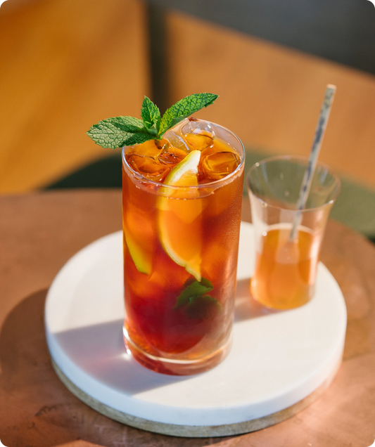 Glass of iced tea with lemon and mint on a white coaster, with another glass in the background.