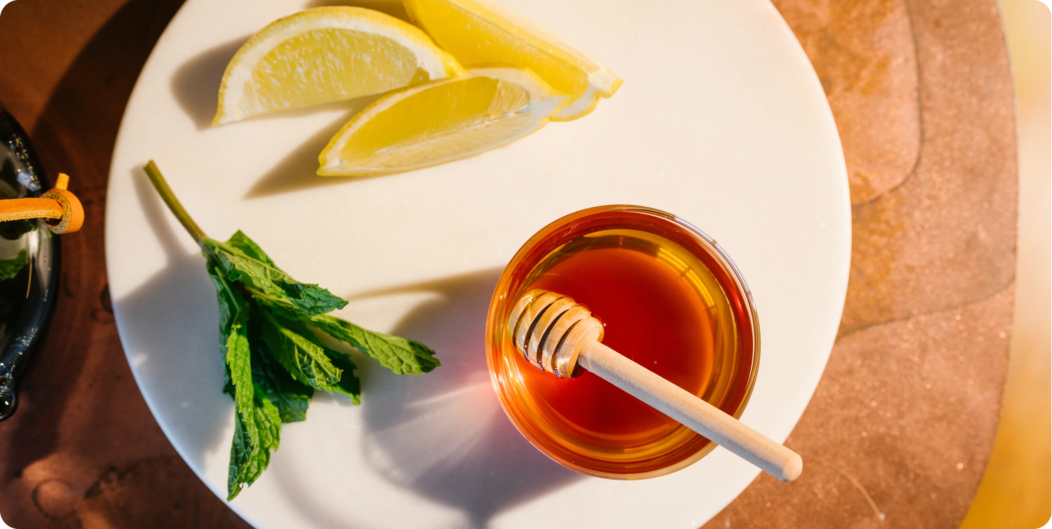Honey dipper in a bowl of honey with lemon slices and mint leaves on a white plate.