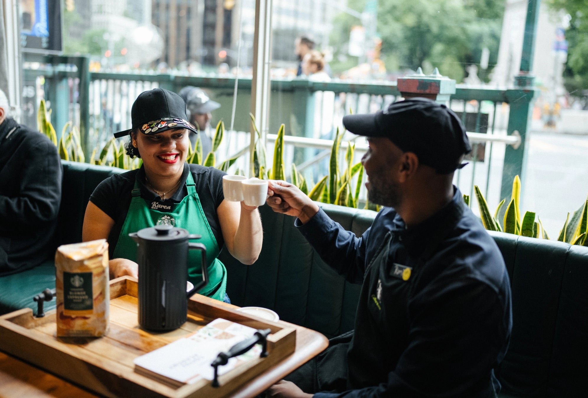 Starbucks barista serving a customer with a tray of coffee and snacks in an outdoor setting.