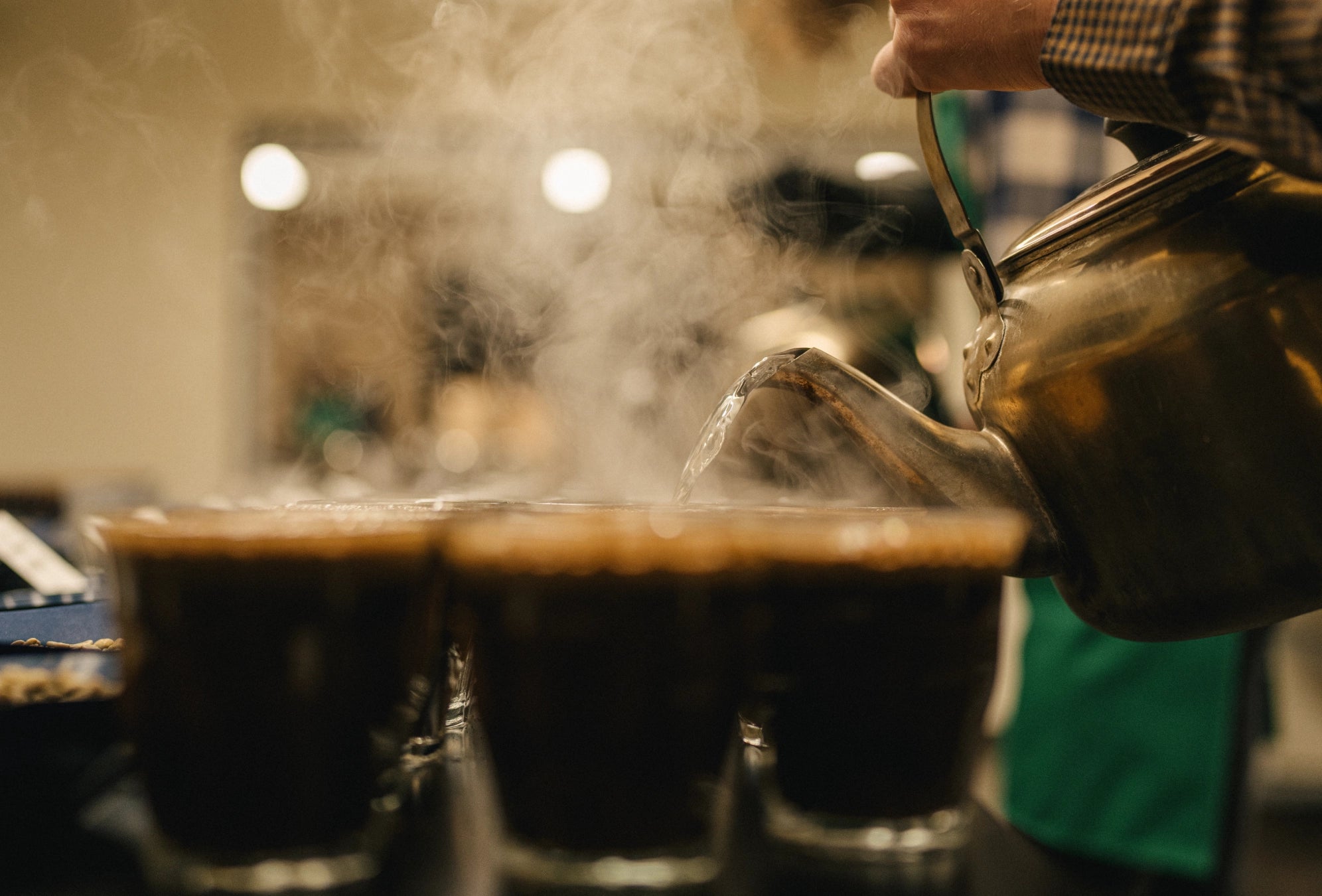 Person pouring steaming hot liquid into cups with a blurred background