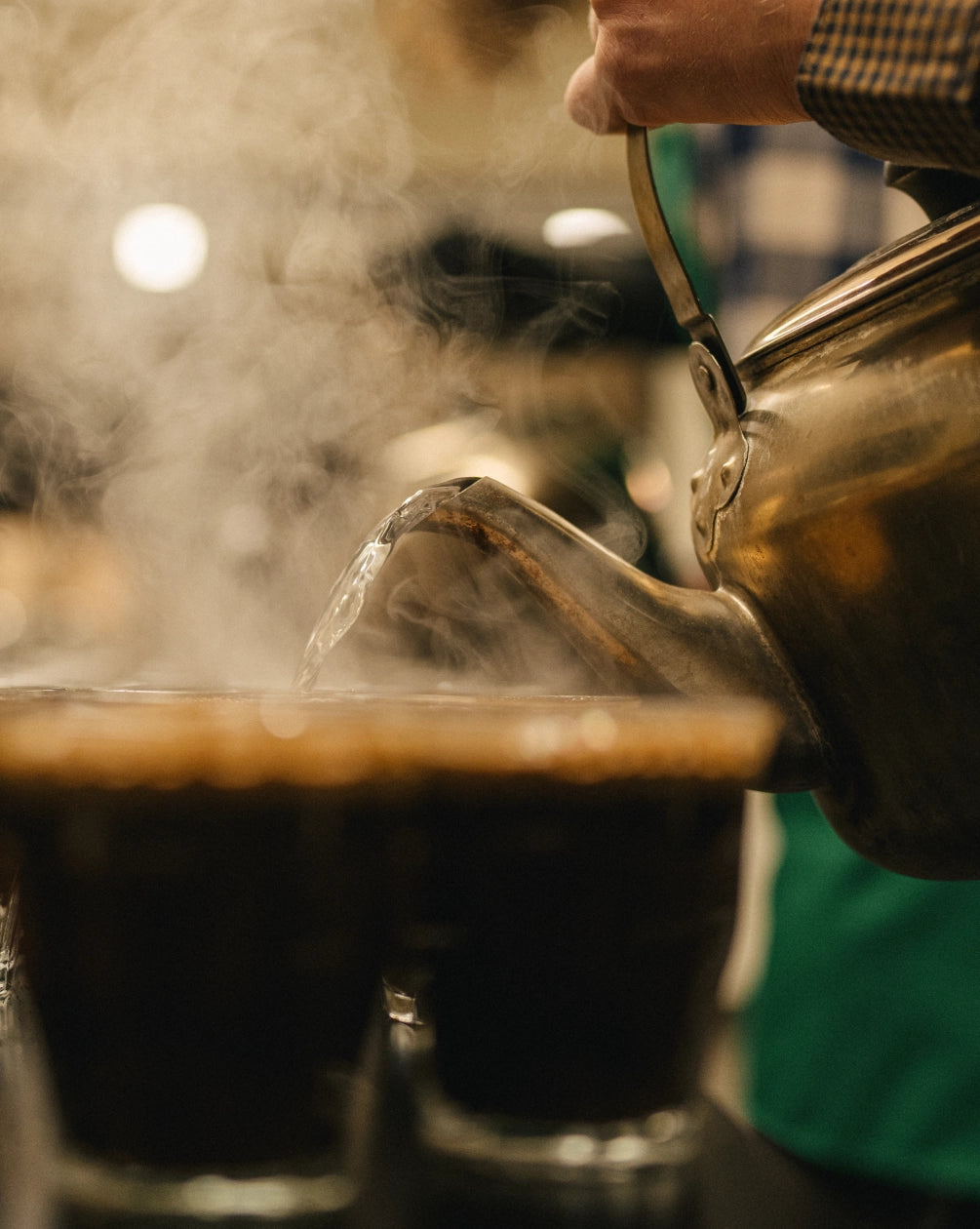 Steaming hot liquid being poured from a teapot into cups with a blurred background