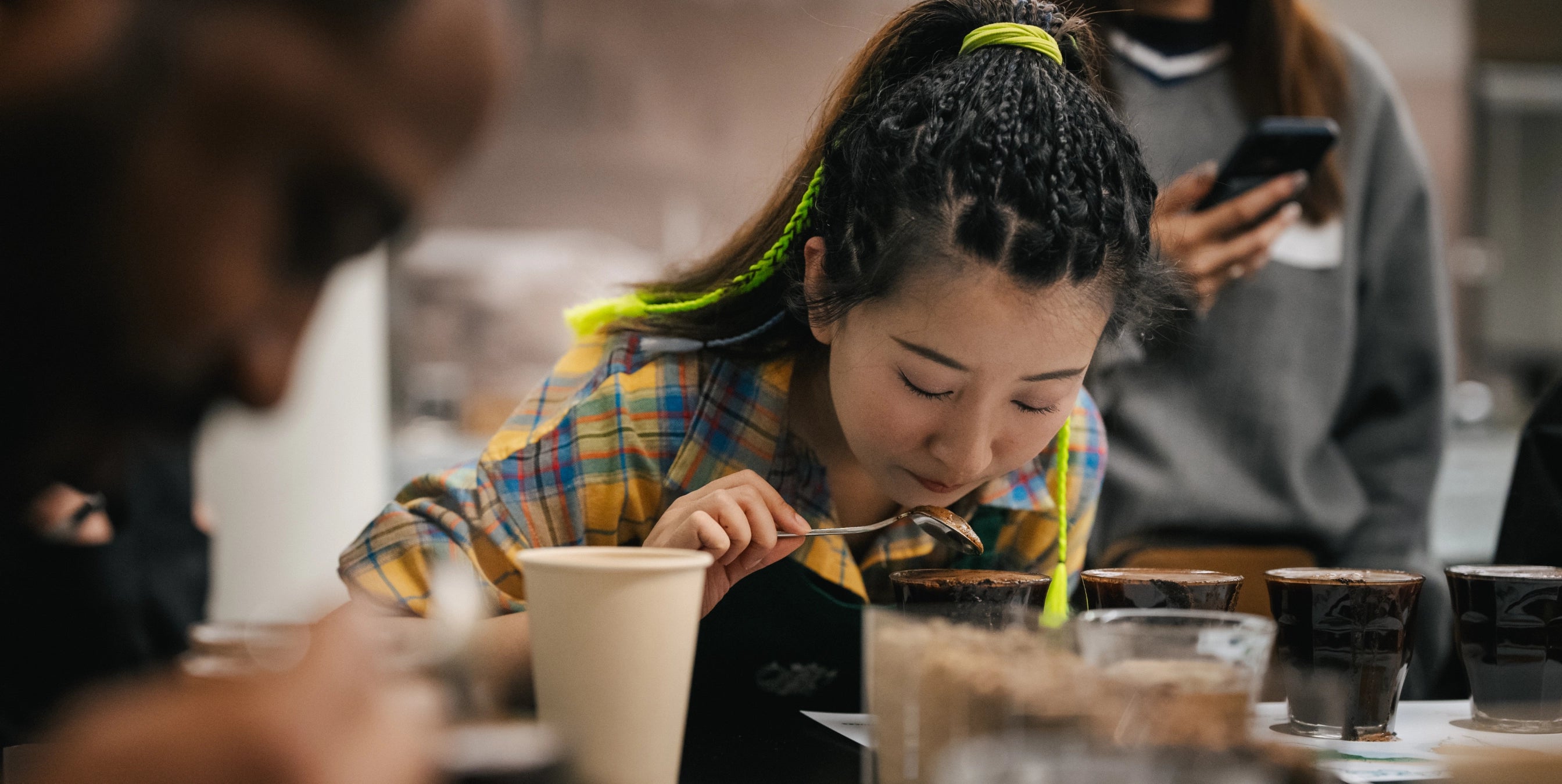 Woman sitting at a table with a cup of coffee, looking down at a smartphone.
