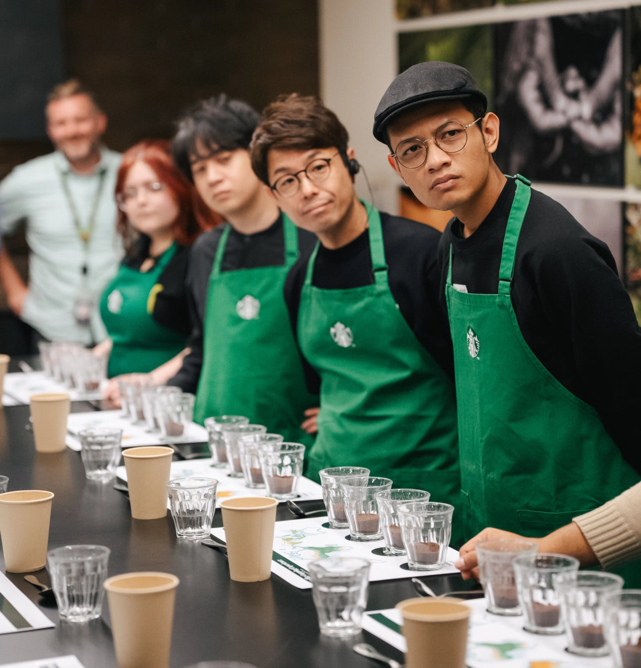 Group of Starbucks employees in green aprons at a table with coffee cups and glasses.