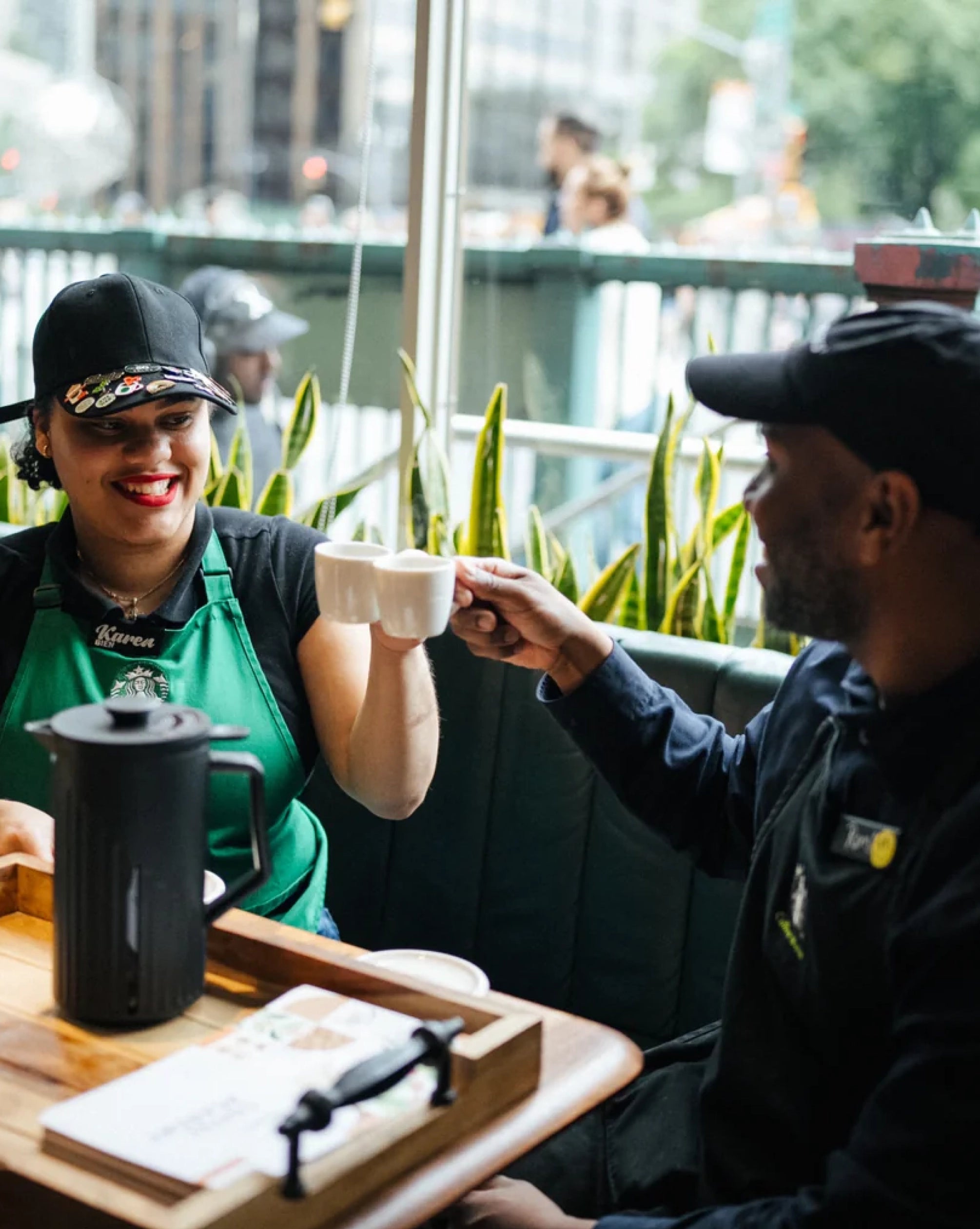 Person in a green apron serving coffee to another person outdoors.