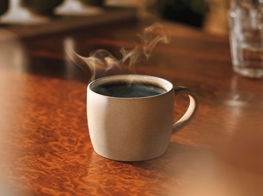 Steaming coffee in a beige mug on a wooden table