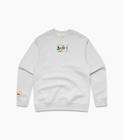 A light heather gray crewneck sweatshirt featuring a small graphic of Snoopy holding a pumpkin on the center chest, with a small orange heart-and-text graphic on the left sleeve.