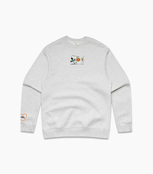 A light heather gray crewneck sweatshirt featuring a small graphic of Snoopy holding a pumpkin on the center chest, with a small orange heart-and-text graphic on the left sleeve.