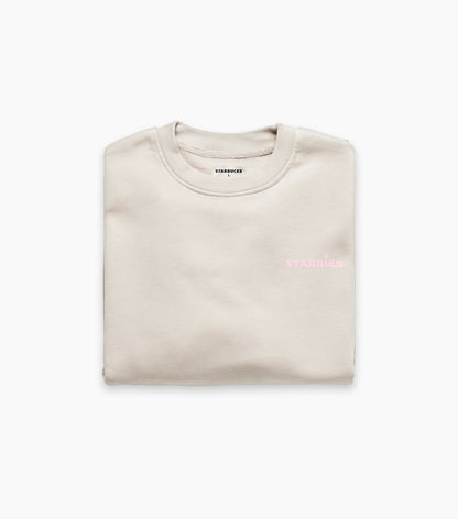 Folded beige crewneck sweatshirt with pink Starbies text on a white background