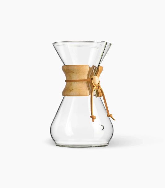 A clear Chemex Glass Pour-Over Coffee Maker, with wooden collar and leather tie against a white background.