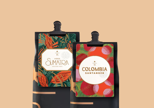 Two black coffee bags clipped at the top, displayed against a warm beige background. 