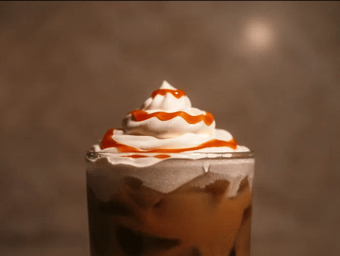 Glass of Salted Caramel Cold Brew with whipped cream and caramel drizzle on a brown background.