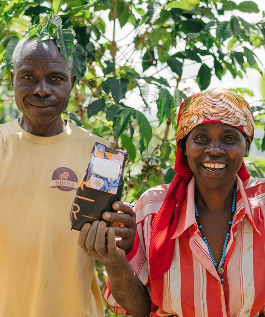 A smiling man and woman stand among coffee plants, and the woman holds up a bag of Starbucks Reserve coffee.