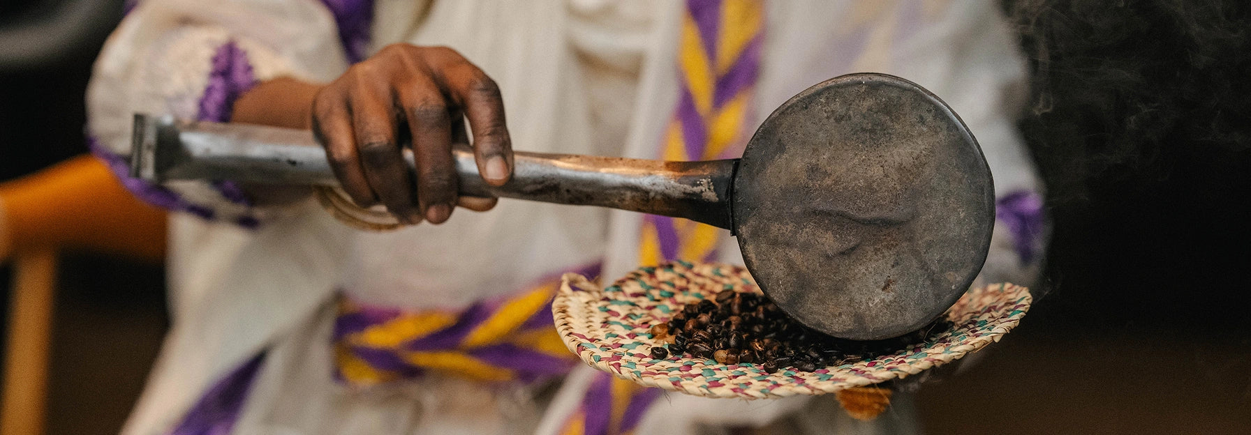 Hand holding a metal object with a textured surface, wearing a traditional garment with purple and yellow accents.
