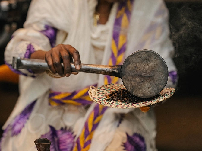 Person holding a traditional pestle and mortar with herbs, wearing a colorful garment.