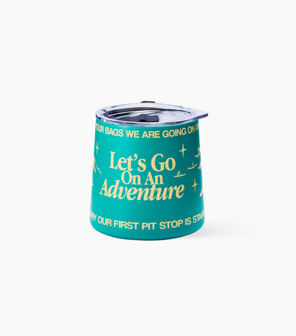 A teal cup with a lid, featuring yellow text that reads 'Let's Go On An Adventure' and other travel-themed phrases, set against a plain white background.