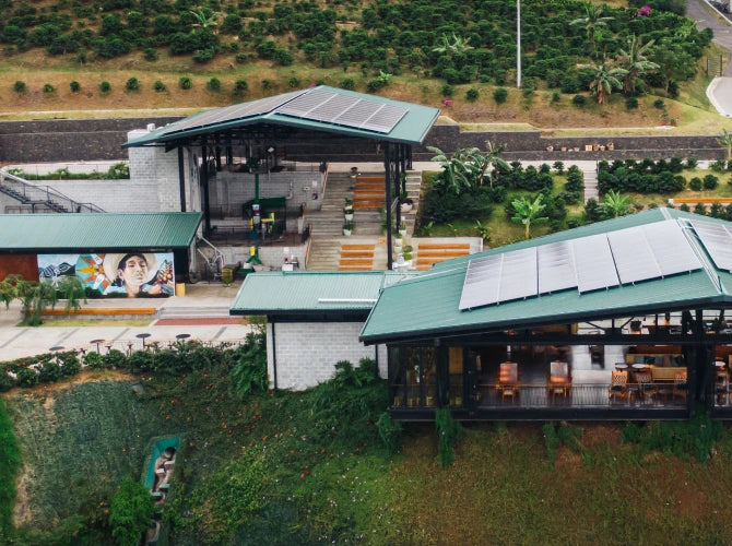 Aerial view of green-roofed buildings with solar panels at Starbucks Hacienda Alsacia coffee farm, surrounded by terraced coffee plants on a hillside in Costa Rica.