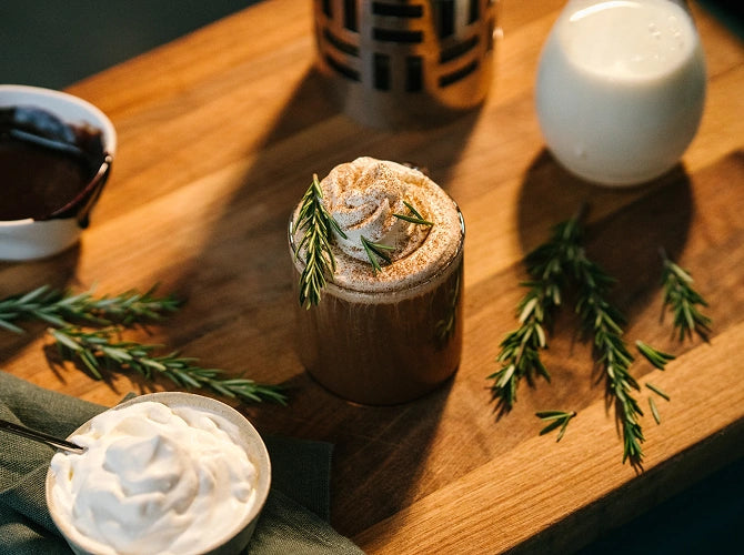 Hot chocolate with whipped cream and rosemary on a wooden table
