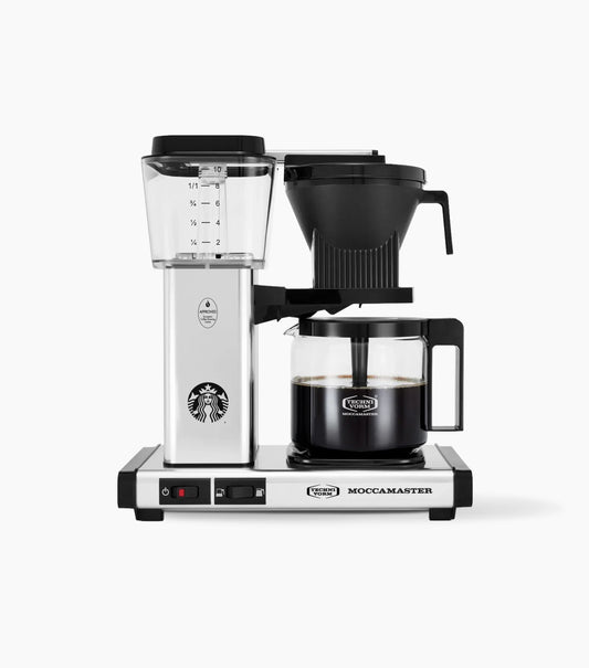A countertop Moccamaster coffee maker with a stainless steel and black body, featuring a clear water reservoir, a black pour-over filter basket, and a glass carafe filled with coffee on a white background.