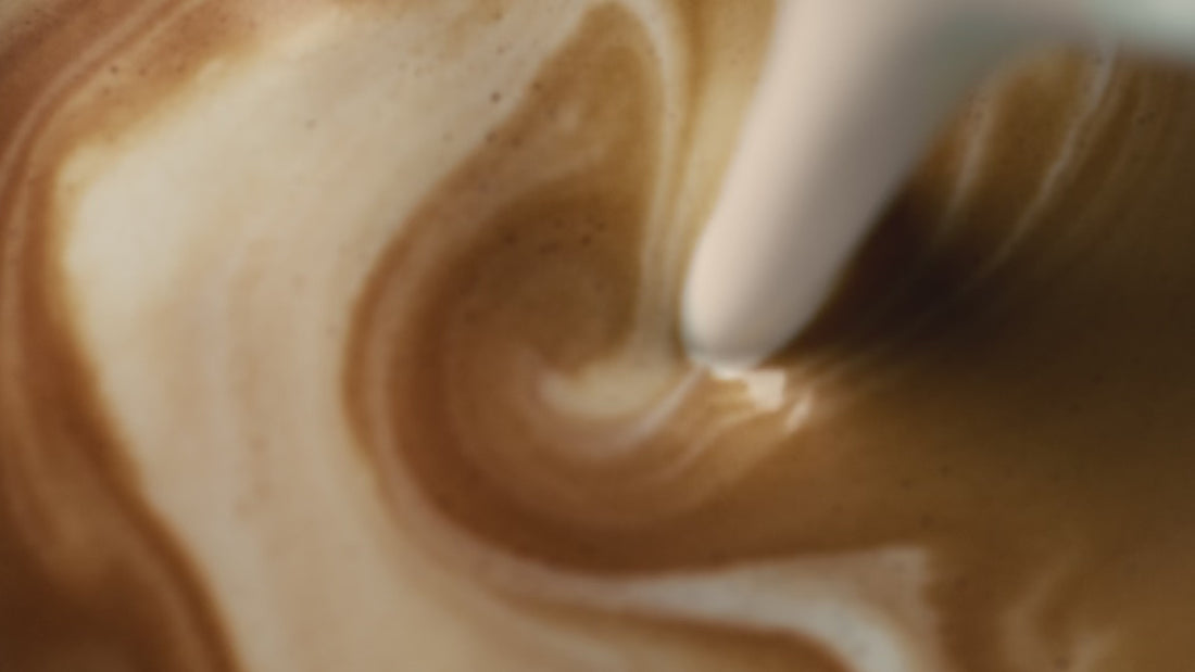 Close-up of milk being poured into coffee in slow motion, creating latte art.