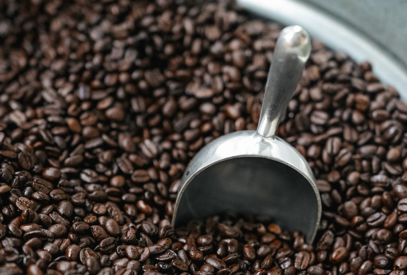 Silver scoop partially buried in roasted coffee beans.