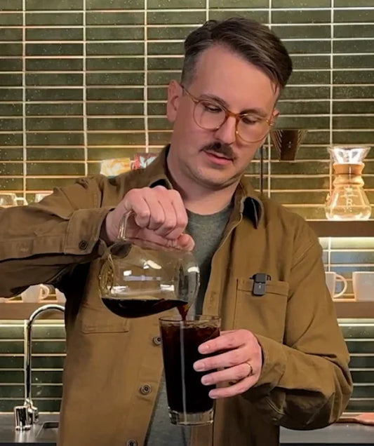 The barista, Lincoln, pouring coffee from a carafe into a glass with ice.