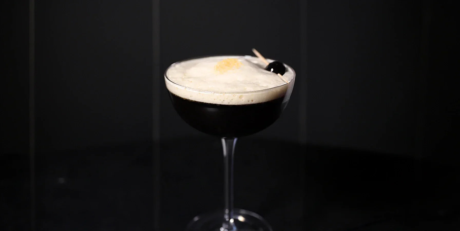 Close-up of a glass of cold brew lemon sour, with a layer of froth and skewer on top.