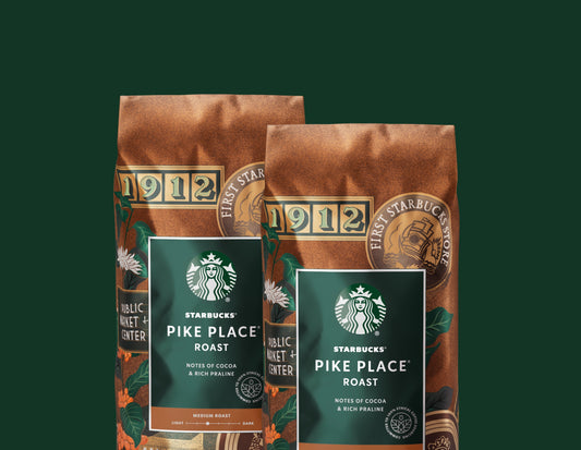 Two bags of Starbucks Pike Place Roast Coffee in front of a light green background.