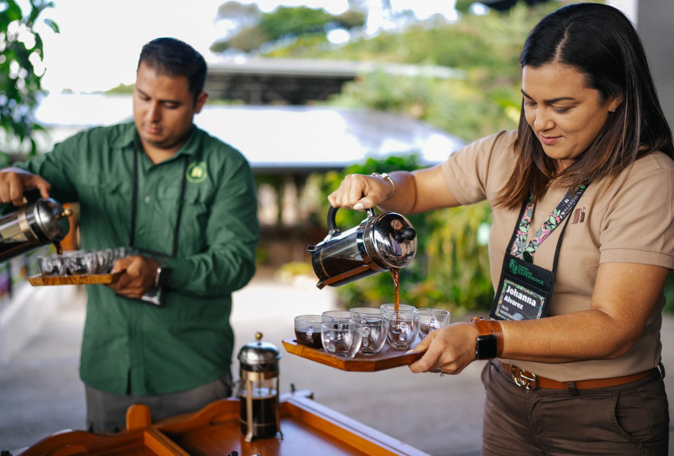 Two people pouring freshly brewed coffee from a French press into glass cups on wooden trays