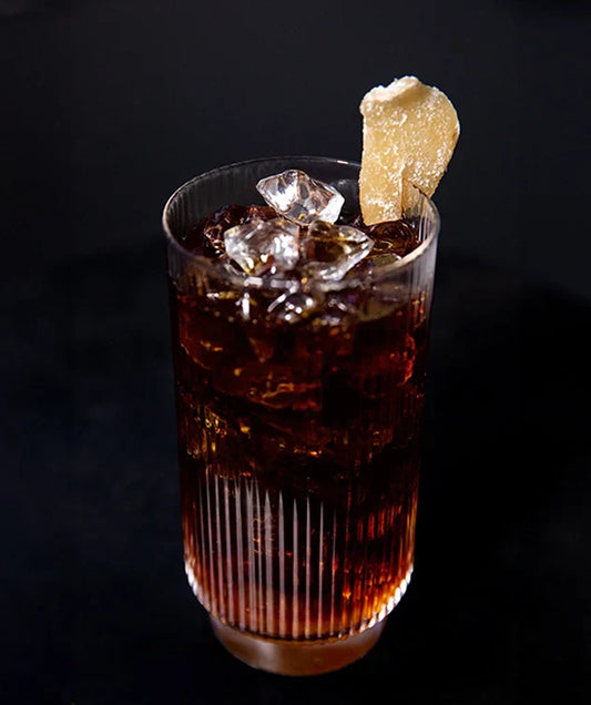 Iced ginger lemon coffee in a drinking glass, with dried candied ginger at the glass edge.