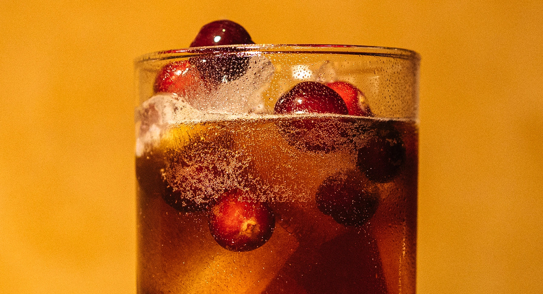 Glass of sparkling drink with berries on a yellow background