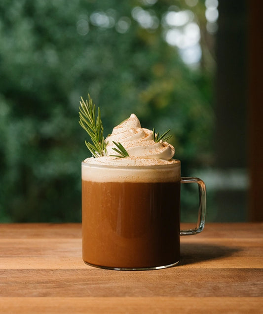 Hot chocolate with whipped cream and a sprig of rosemary on a wooden table.