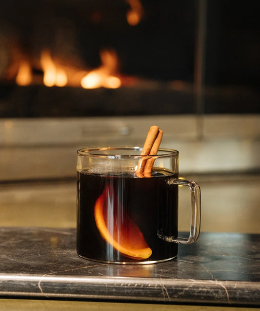 Glass mug of hot drink with cinnamon stick on a table in front of a fireplace